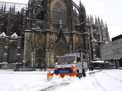 AWB Wagen mit Schneeschieber räumt Schnee auf der vollgeschneiten Domplatte mit Dom im Hintergrund. 